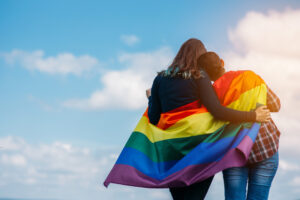 same-sex couple hugging with LGBTQ+ flag
